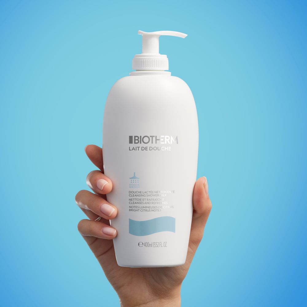 Eine Hand halt eine Lotionflasche vor einem blauen Hintergrund.