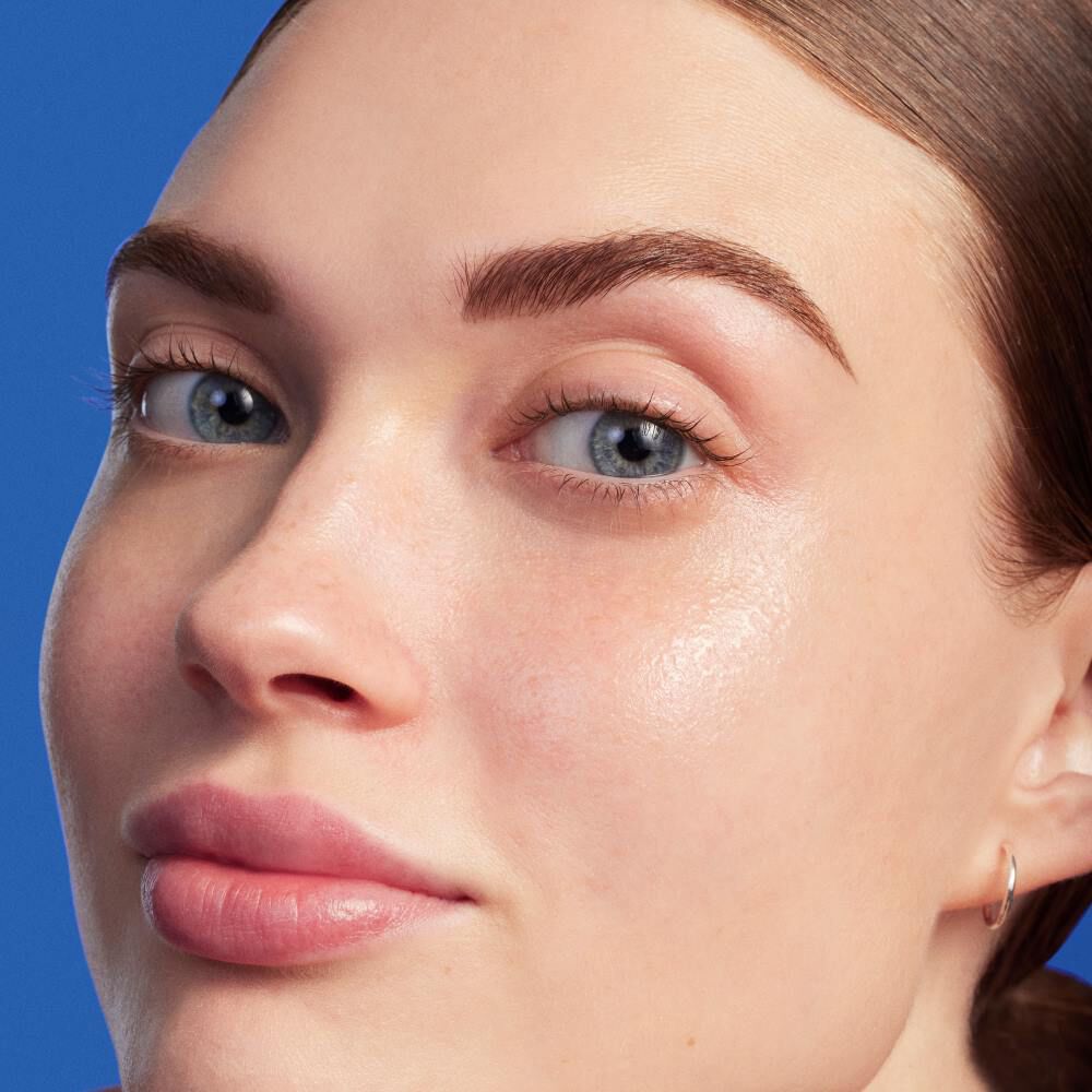 Frau mit glanzender Haut lachelt leicht, blauer Hintergrund.