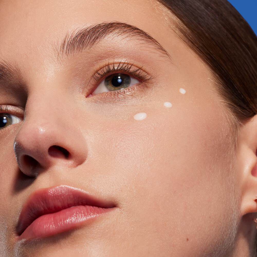 Gesicht mit Creme unter den Augen, entspannter Ausdruck, vor neutralem Hintergrund.