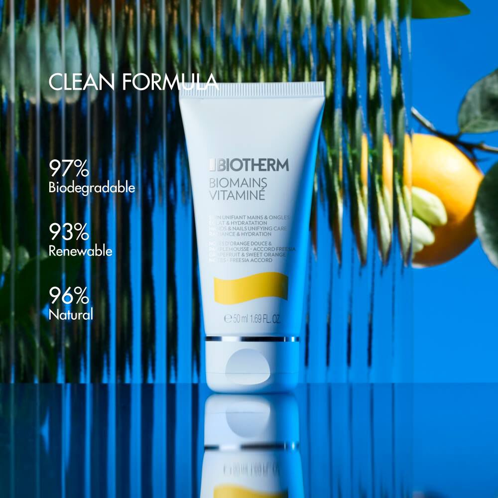 Sonnencremetube reflektiert im Wasser, umgeben von grunen Blattern und einer halben Zitrone.