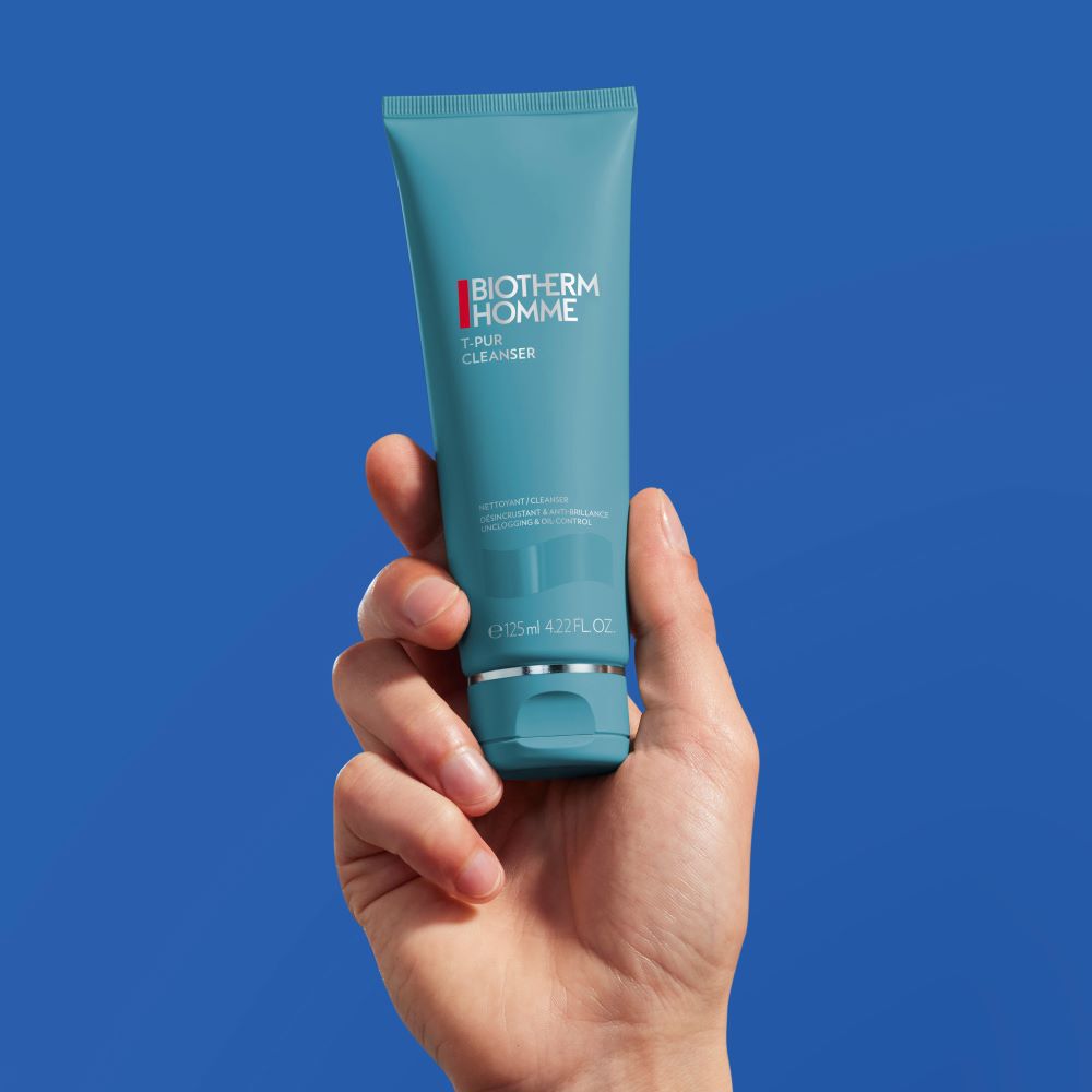 Eine Hand halt eine blaue Tube vor blauem Hintergrund. Text: "Face Cleanser Detox, Protect."