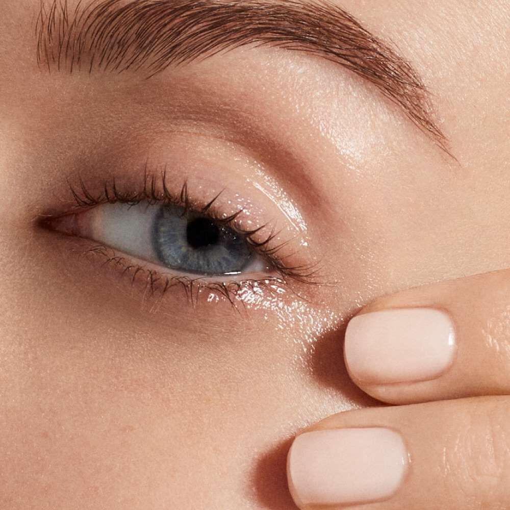 Ein Auge mit hellblauer Iris, eine Hand mit hellrosa lackierten Fingern beruhrt sanft die Haut darunter.