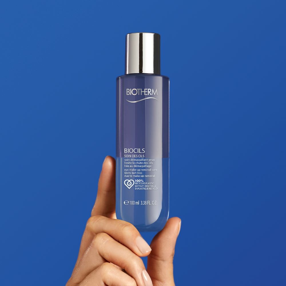 Hand halt eine transparente Flasche mit silbernem Deckel vor blauem Hintergrund.