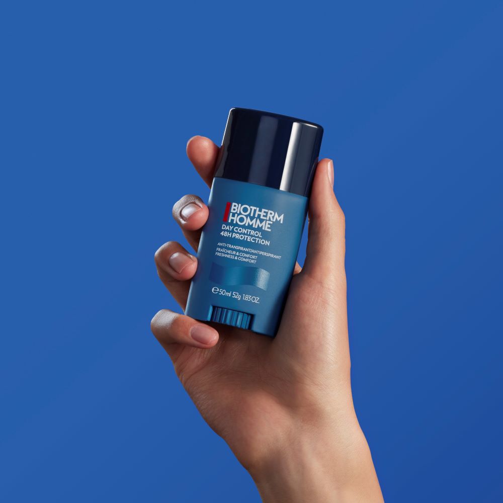 Eine Hand halt ein blaues Deodorant vor einfarbig blauem Hintergrund.