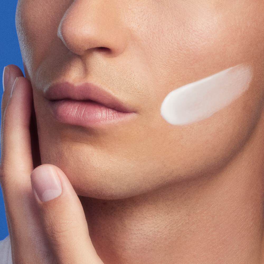 Eine Person tragt Creme auf die Wange auf, Hintergrund in Blau.