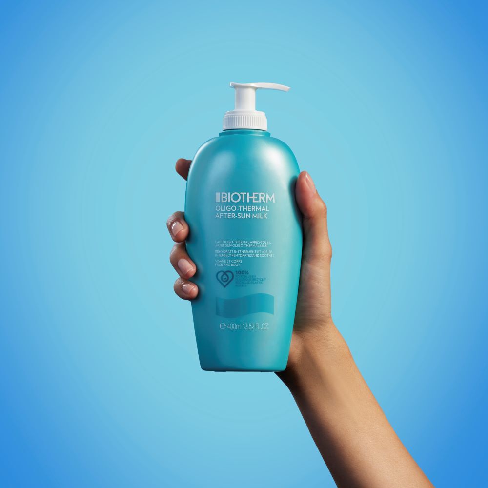 Eine Hand halt eine blaue Lotionflasche mit Spender vor blauem Hintergrund.