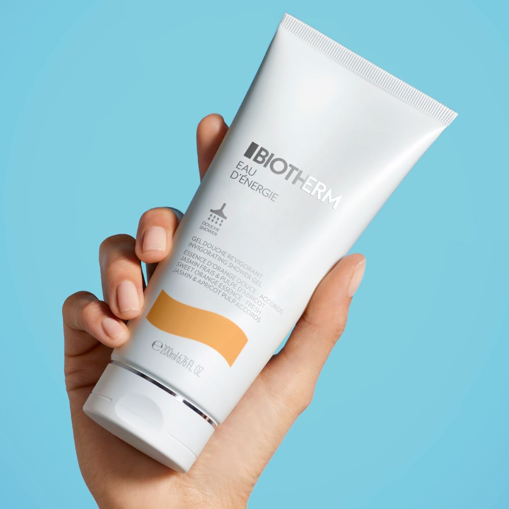 Eine Hand halt eine Tube Hautpflegecreme vor blauem Hintergrund.