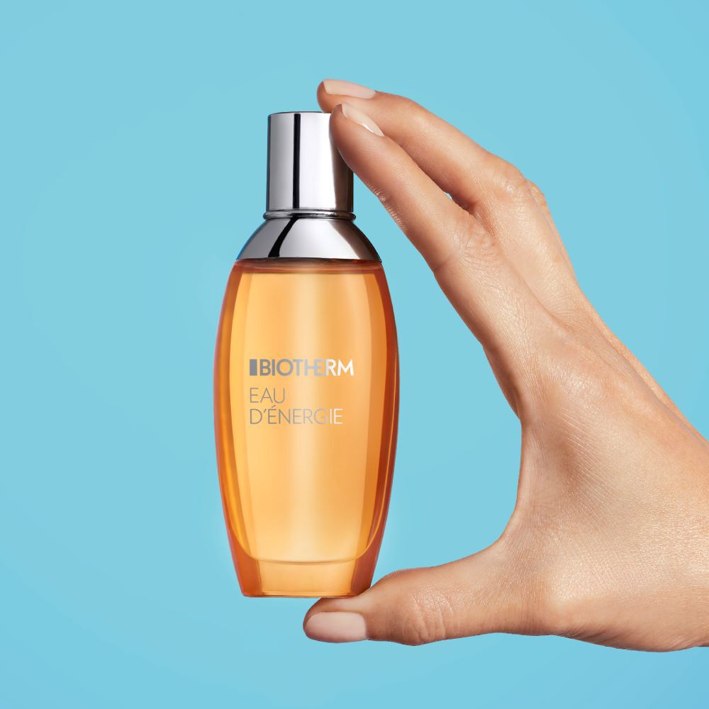 Hand halt Parfumflasche vor blauem Hintergrund.