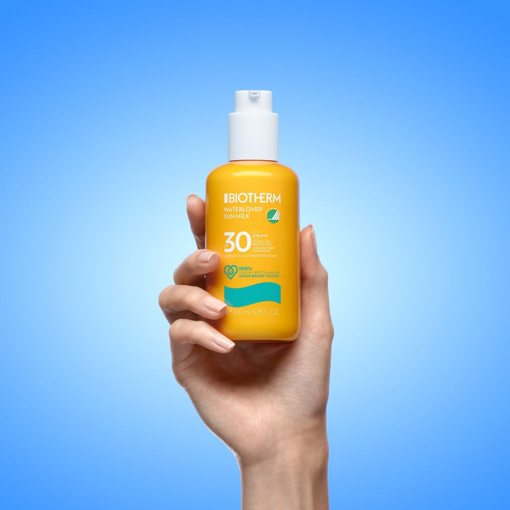 Hand halt Sonnenschutzflasche vor blauem Hintergrund.