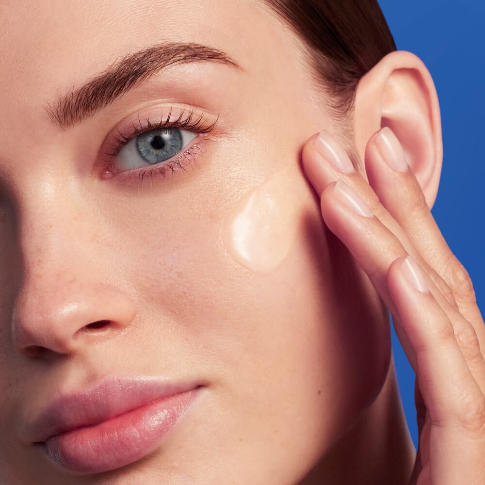 Person tragt Creme auf, in Nahaufnahme, vor blauem Hintergrund.