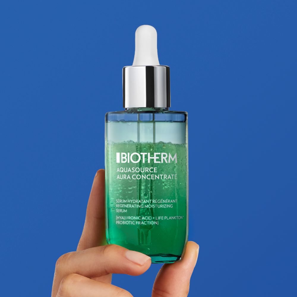 Flasche Serum wird in der Hand gehalten vor blauem Hintergrund. Text: "GLOW RECIPE Plum Plump".