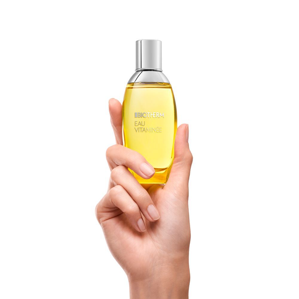 Hand halt gelbes Parfumflaschchen mit silbernem Spruhkopf vor weißem Hintergrund.
