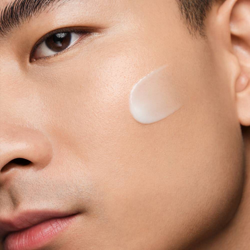 Gesicht mit Cremefleck auf der Wange, Nahaufnahme, Fokus auf Hautpflege im Innenraum.