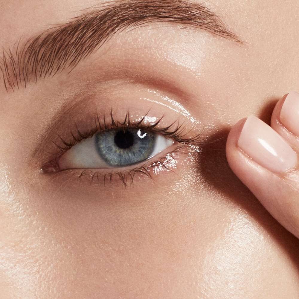 Ein Auge wird von einer Hand beruhrt, nahes Gesicht, neutrale Hintergrundfarbe.