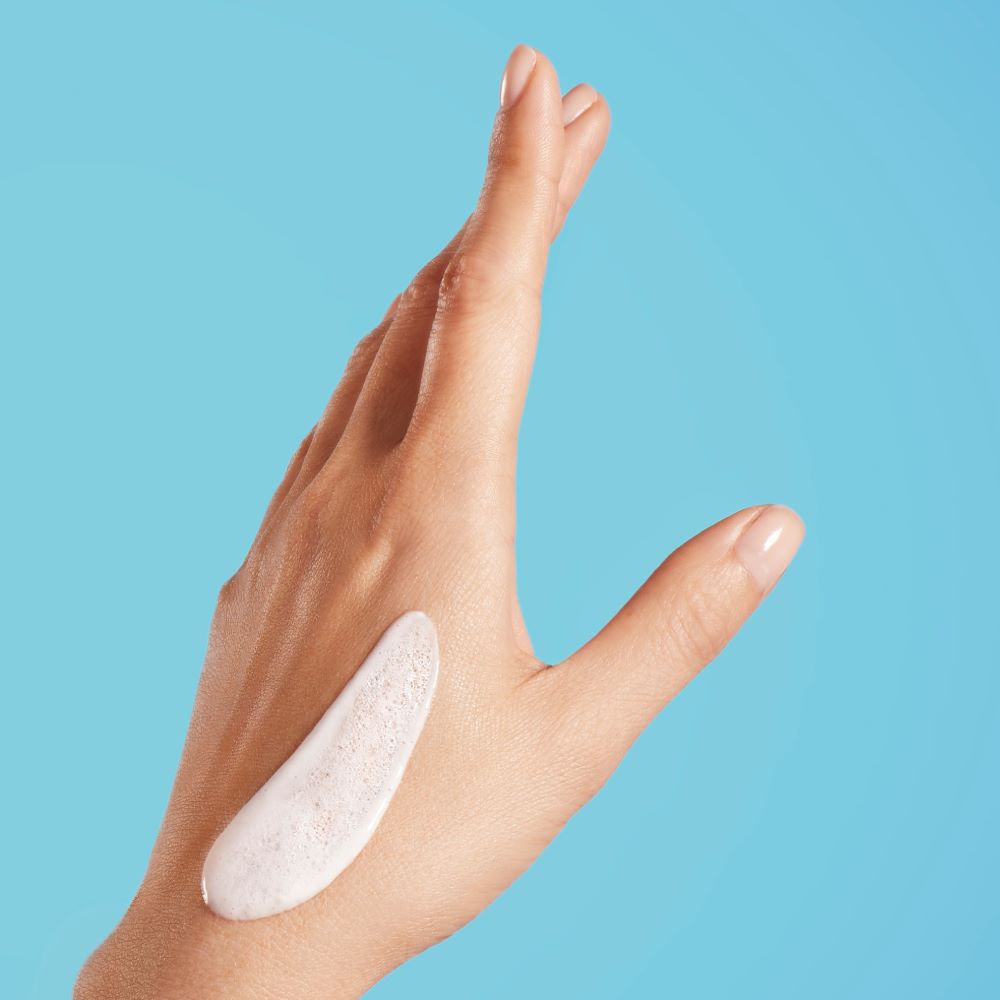 Hand mit weißer Creme, ausgestreckt vor blauem Hintergrund.